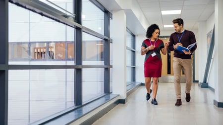Two teachers are walking and talking together down the school hall. They are discussing a student's work.