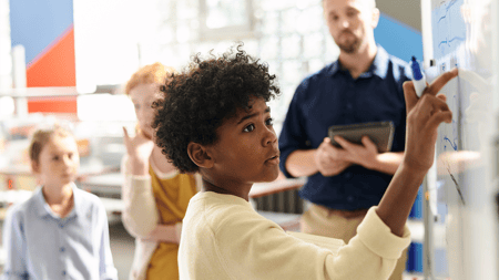 Pensive schoolkid solving equation on whiteboard in class