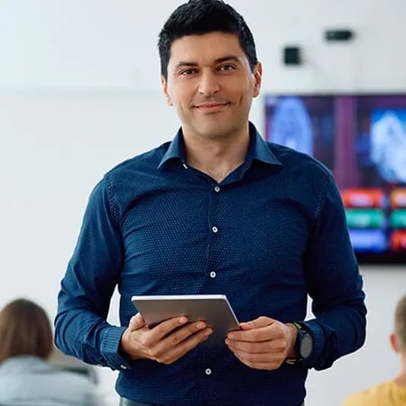 Happy teacher with touchpad during computer class at high school looking at camera.