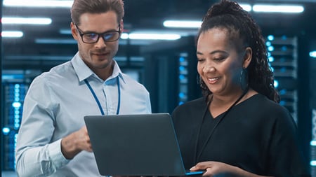 two people looking at a laptop in a server room