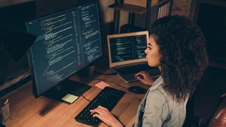 woman sitting in front of two screens with code