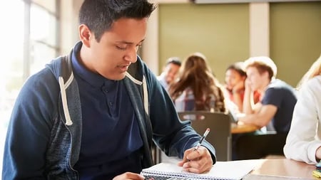 Male High School Student With Calculator Working At Desk