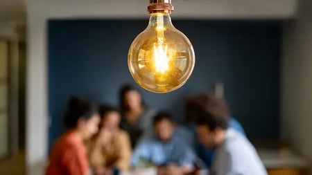 close-up of a light bulb with a marketing team collaborating in the background