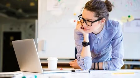 Woman with glasses and hair up stares intently at a computer