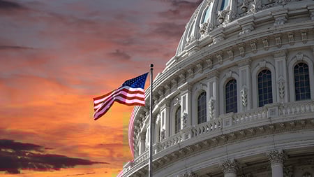 American flag flying above the capital rotunda against a yellow sky