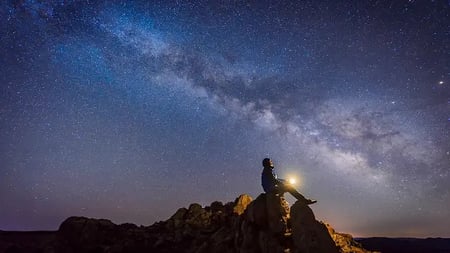 Man sitting under The Milky Way Galaxy with light on his hands