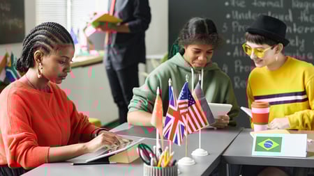 Students in a classroom sitting around a table on tablets with world flags in the middle