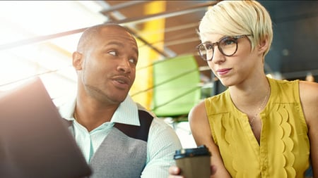 Two people sitting together in an office setting discussing over coffee