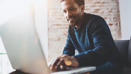 Cheerful African man using computer and smiling while sitting on the sofa.