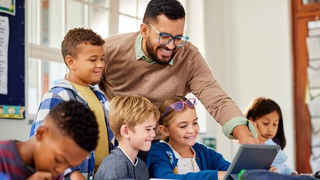 Cheerful male teacher helping students using digital tablet in classroom during technology lesson