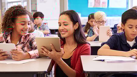 Teacher with tablet showing a student an assignment at her desk.